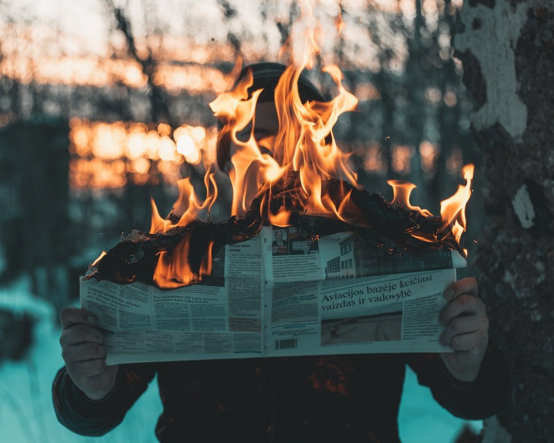 A person holding a newspaper in front of a fire