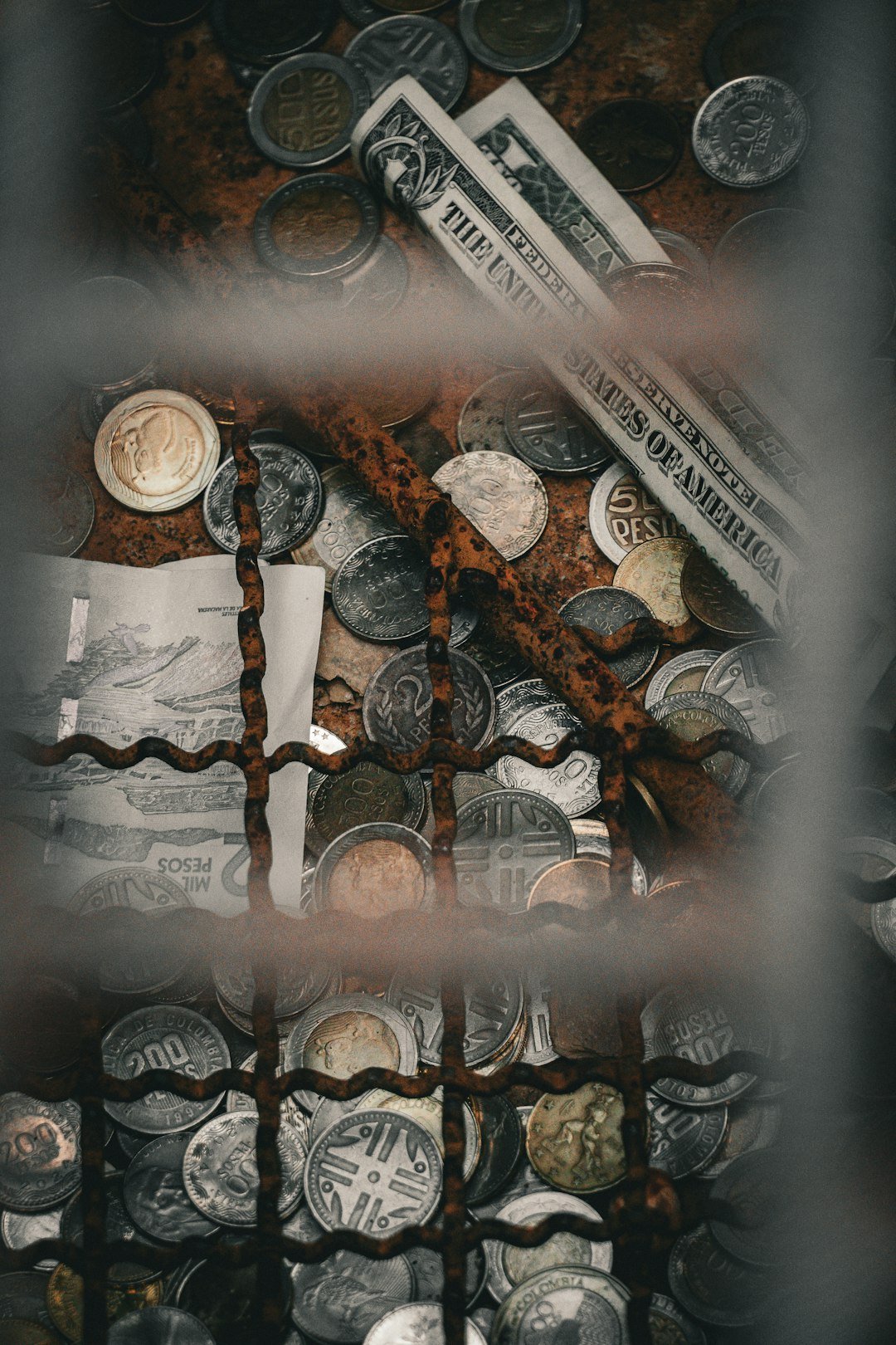 Us dollar bills and various coins behind a rusty grate.