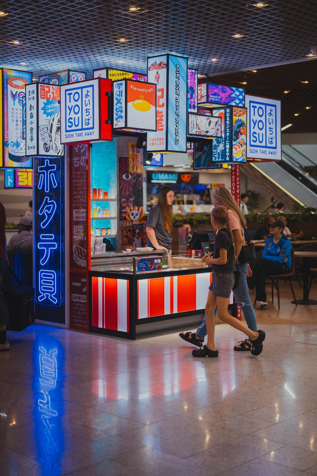 People walk past a brightly lit japanese food stall.