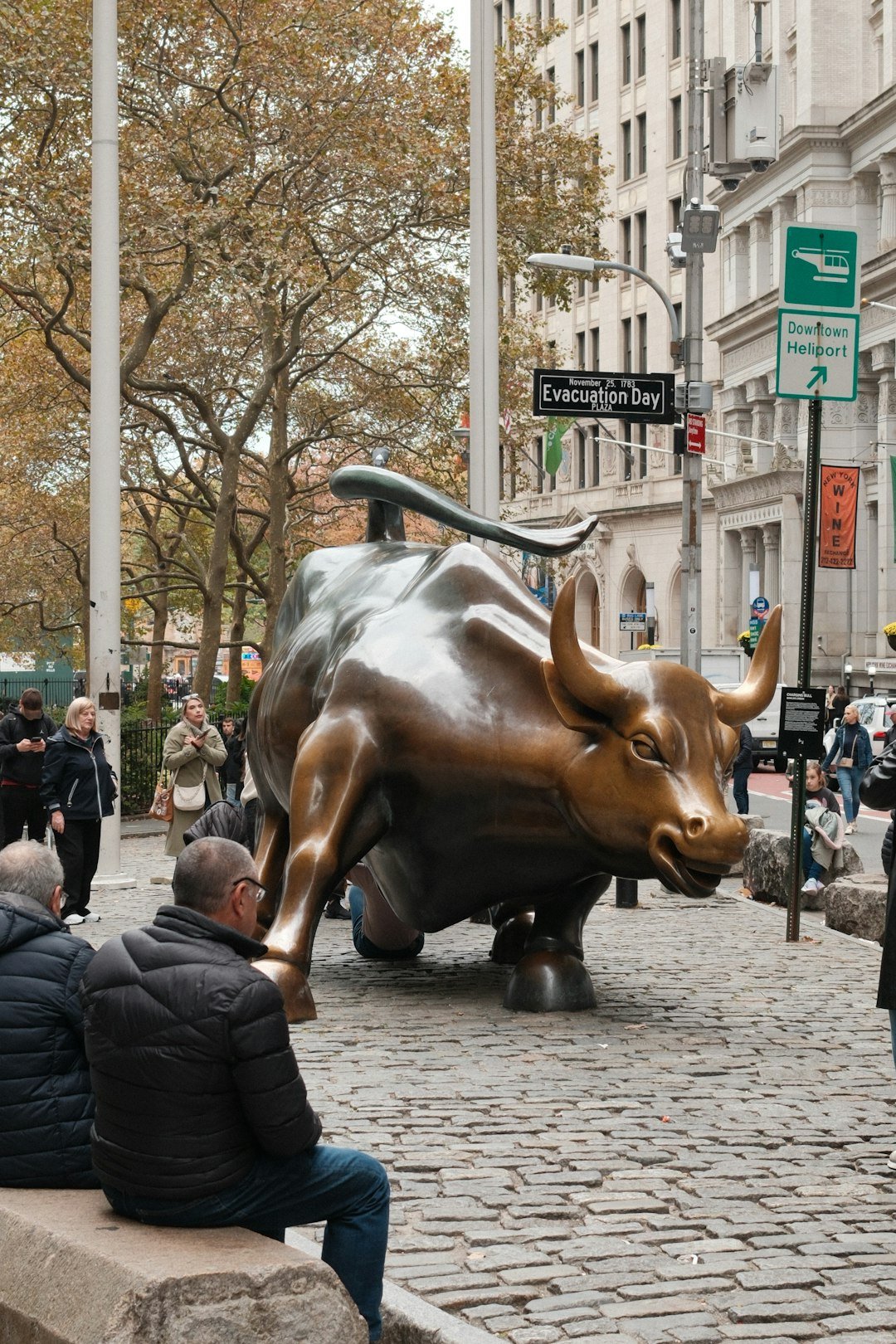 Charging bull statue on cobblestone street with onlookers